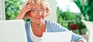 Image of senior woman wearing eye glasses in front of laptop reading an accessible healthcare insurance document.