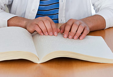 Image of student at a desk reading a braille textbook.